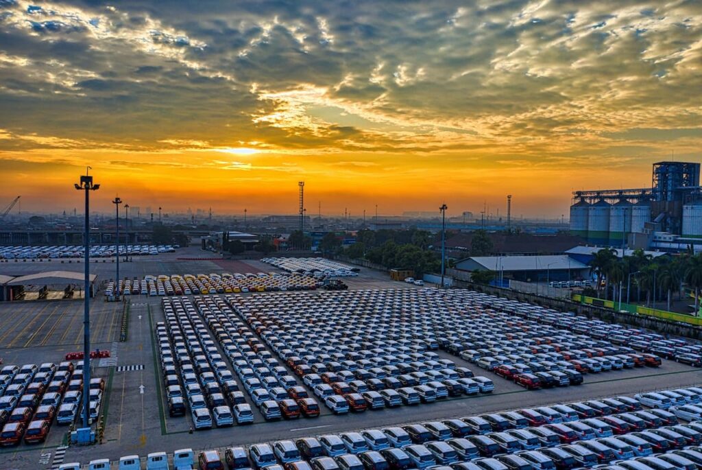 une centaine de véhicules de flotte automobile garés sur un parking avec un couchés de soleil en arrière plan