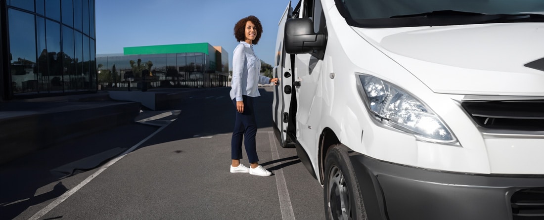 Femme ouvrant un véhicule utilitaire partagé sur un parking d'entreprise, illustrant la mobilité professionnelle flexible